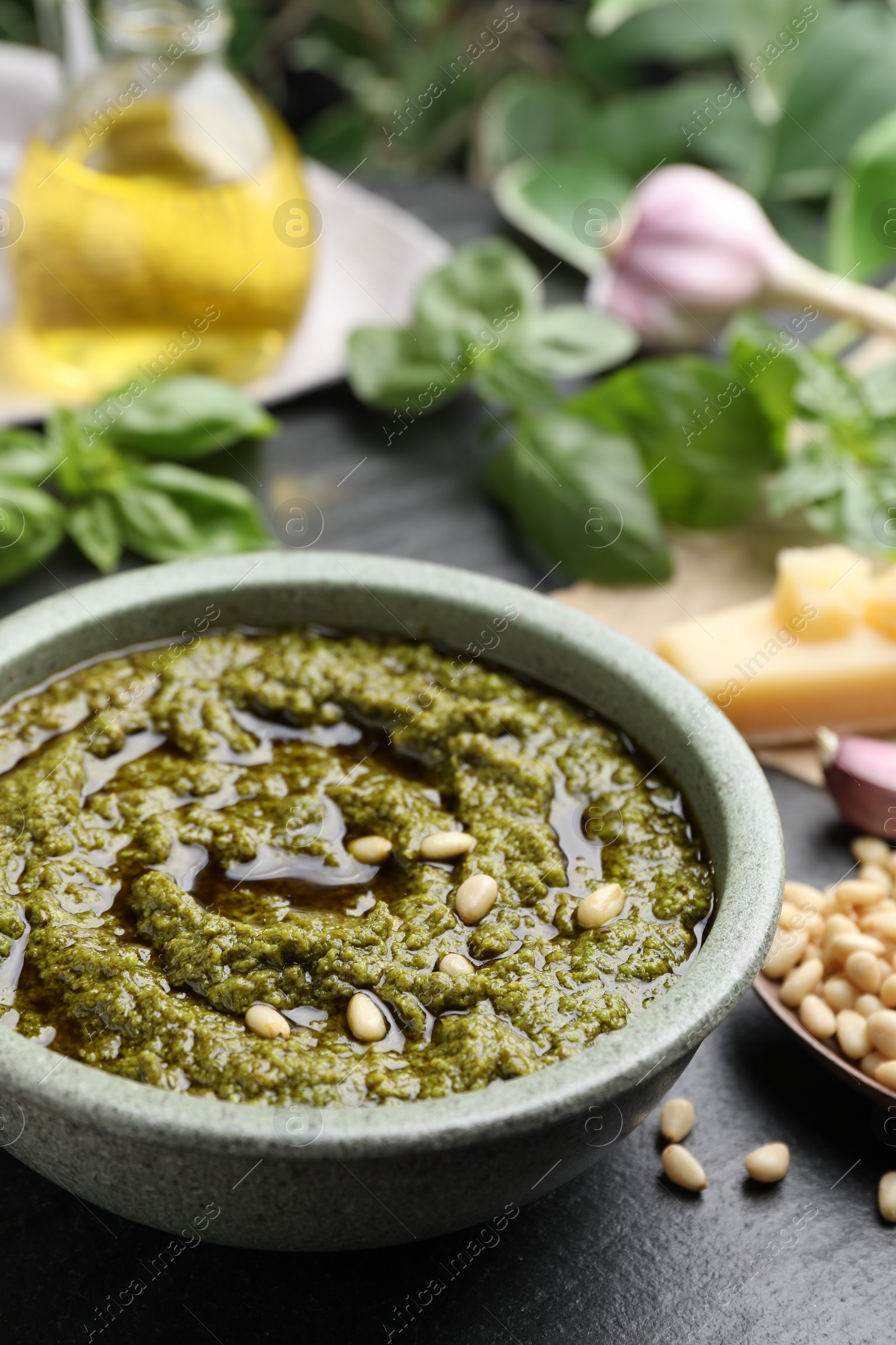 Photo of Tasty pesto sauce in bowl and pine nuts on black table, closeup