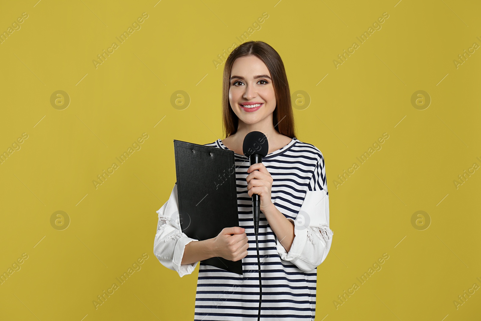 Photo of Young female journalist with microphone and clipboard on yellow background