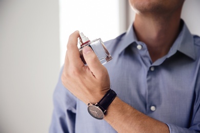 Young man with bottle of perfume indoors, closeup