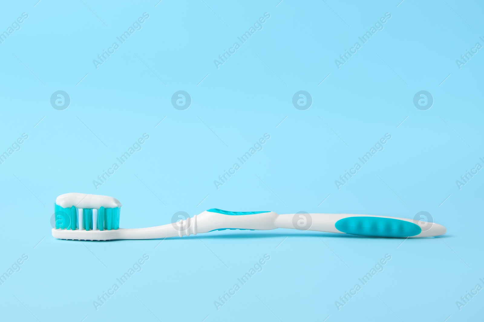 Photo of Brush with toothpaste on light blue background, space for text
