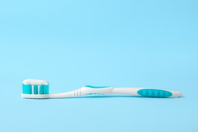 Brush with toothpaste on light blue background, space for text