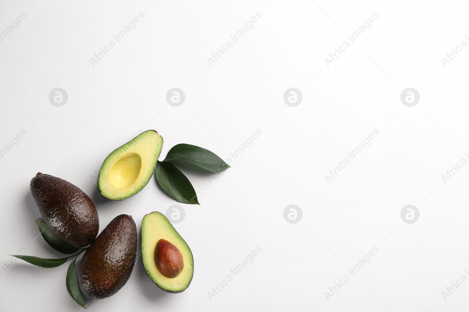 Photo of Whole and cut ripe avocadoes with green leaves on white background, top view