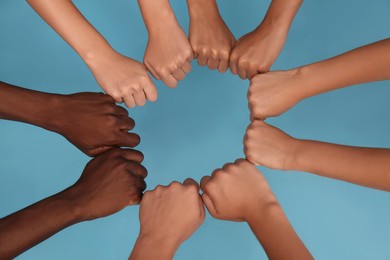 Photo of Group of multiracial people joining fists together on light blue background, closeup