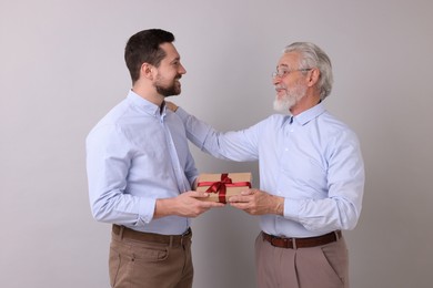 Photo of Son giving gift box to his dad on gray background
