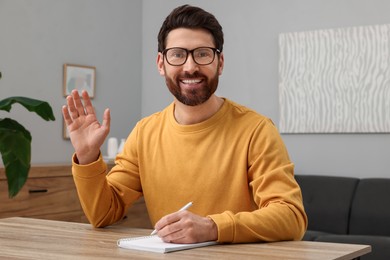 Photo of Man in glasses greeting someone at wooden table indoors