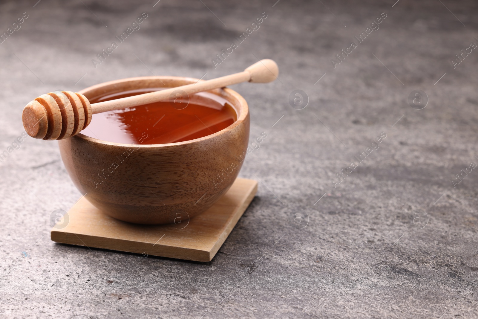 Photo of Delicious honey in bowl and dipper on grey textured table. Space for text