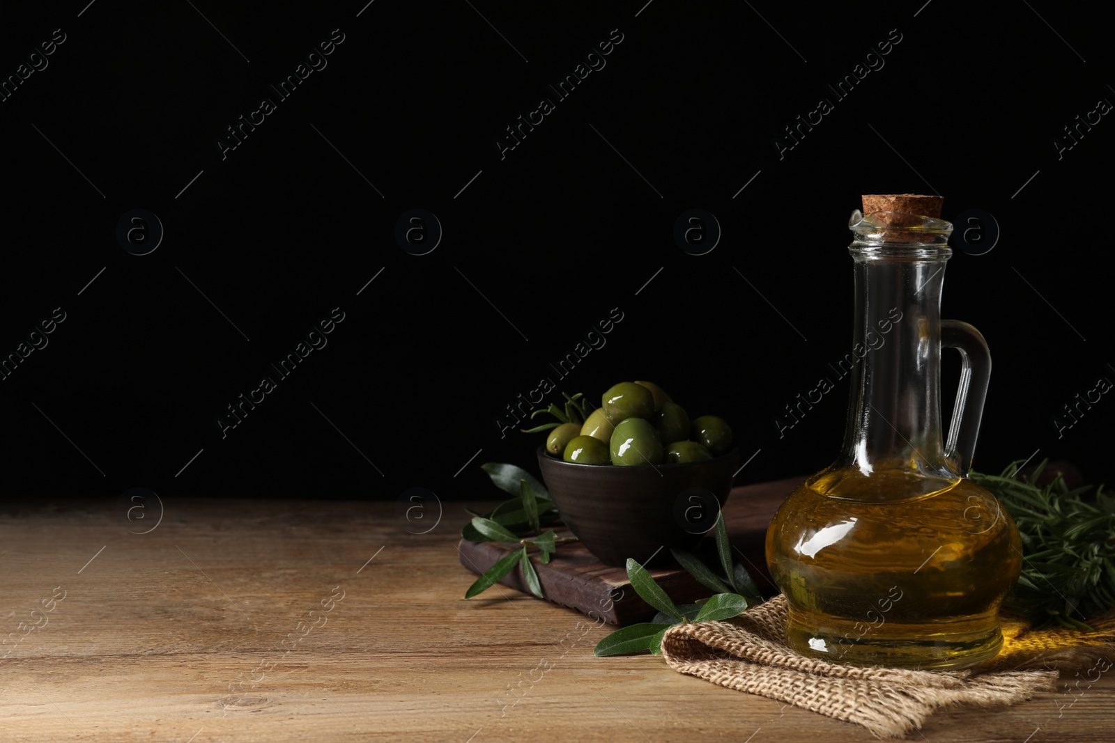 Photo of Glass jug of oil, ripe olives and green leaves on wooden table. Space for text