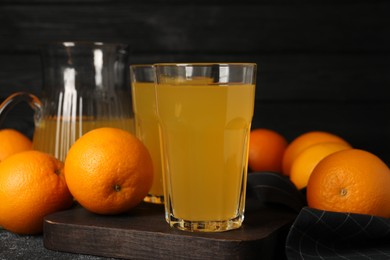 Photo of Many ripe oranges and fresh juice on dark grey table