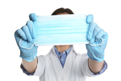 Photo of Doctor in latex gloves holding disposable face mask on white background, closeup. Protective measures during coronavirus quarantine