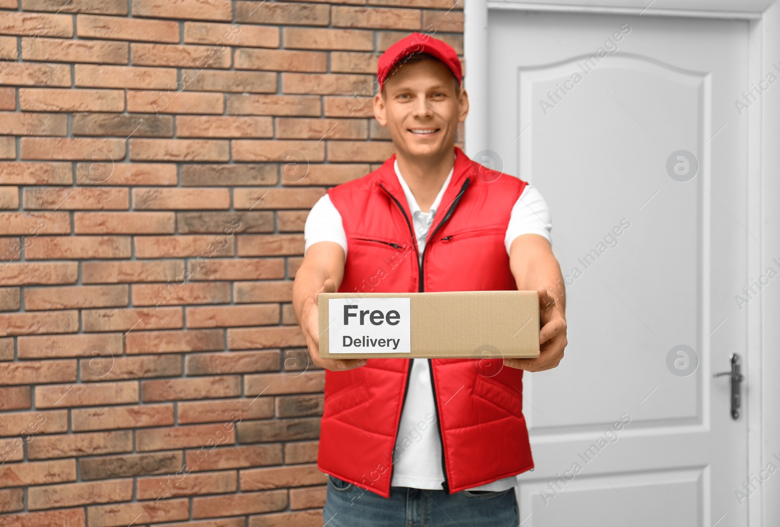 Photo of Courier holding parcel with sticker Free Delivery indoors
