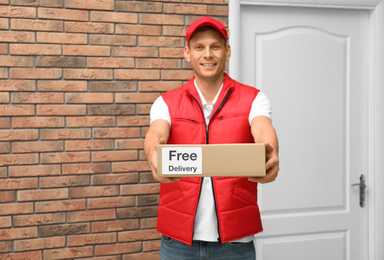 Photo of Courier holding parcel with sticker Free Delivery indoors