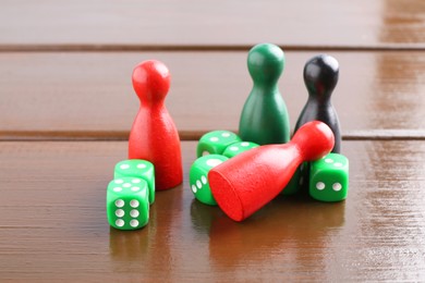 Green dices and color game pieces on wooden table, closeup