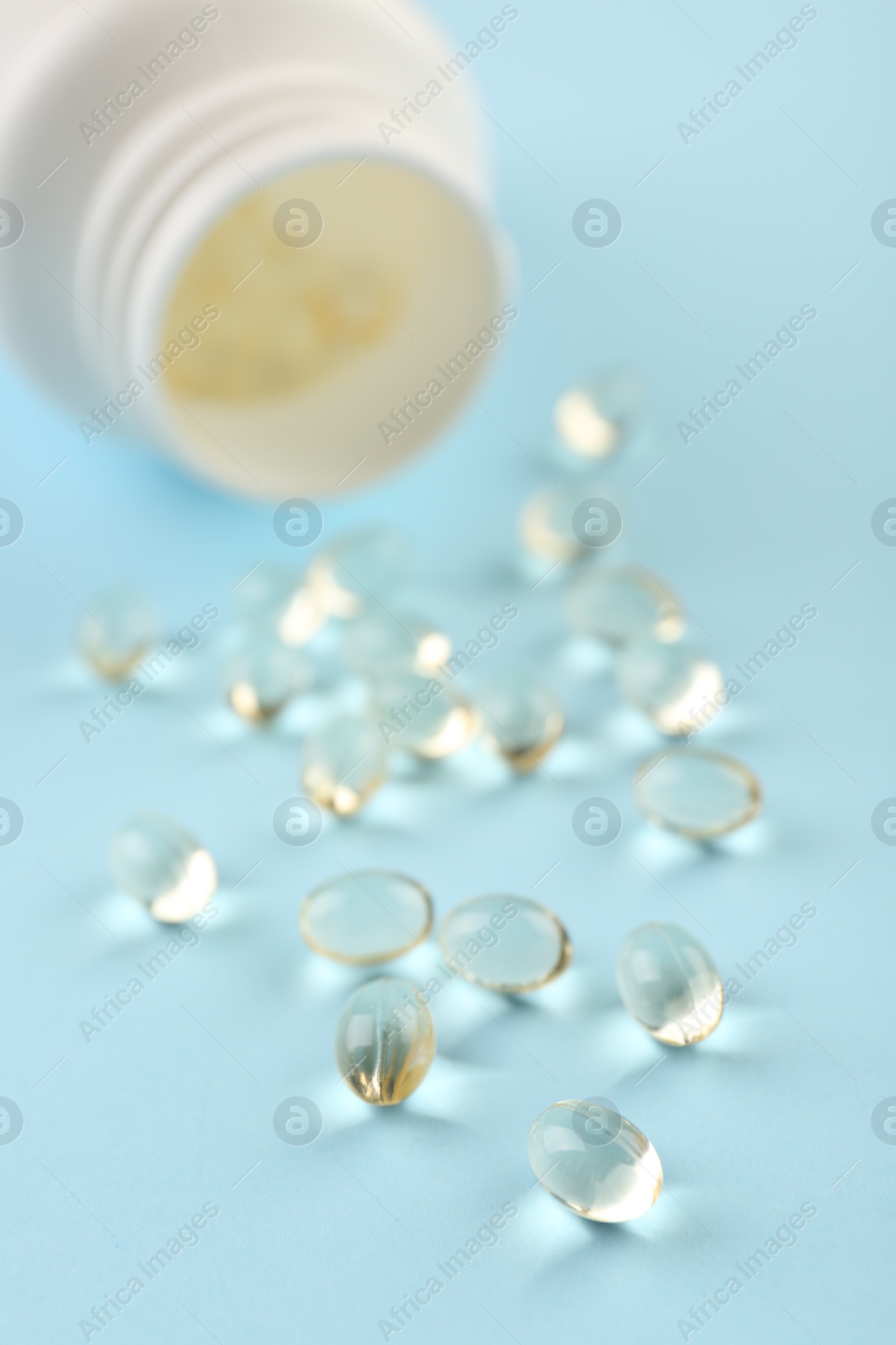 Photo of Bottle and vitamin capsules on light blue background, closeup