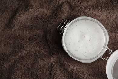 Photo of Jar of salt scrub on brown towel, top view. Space for text