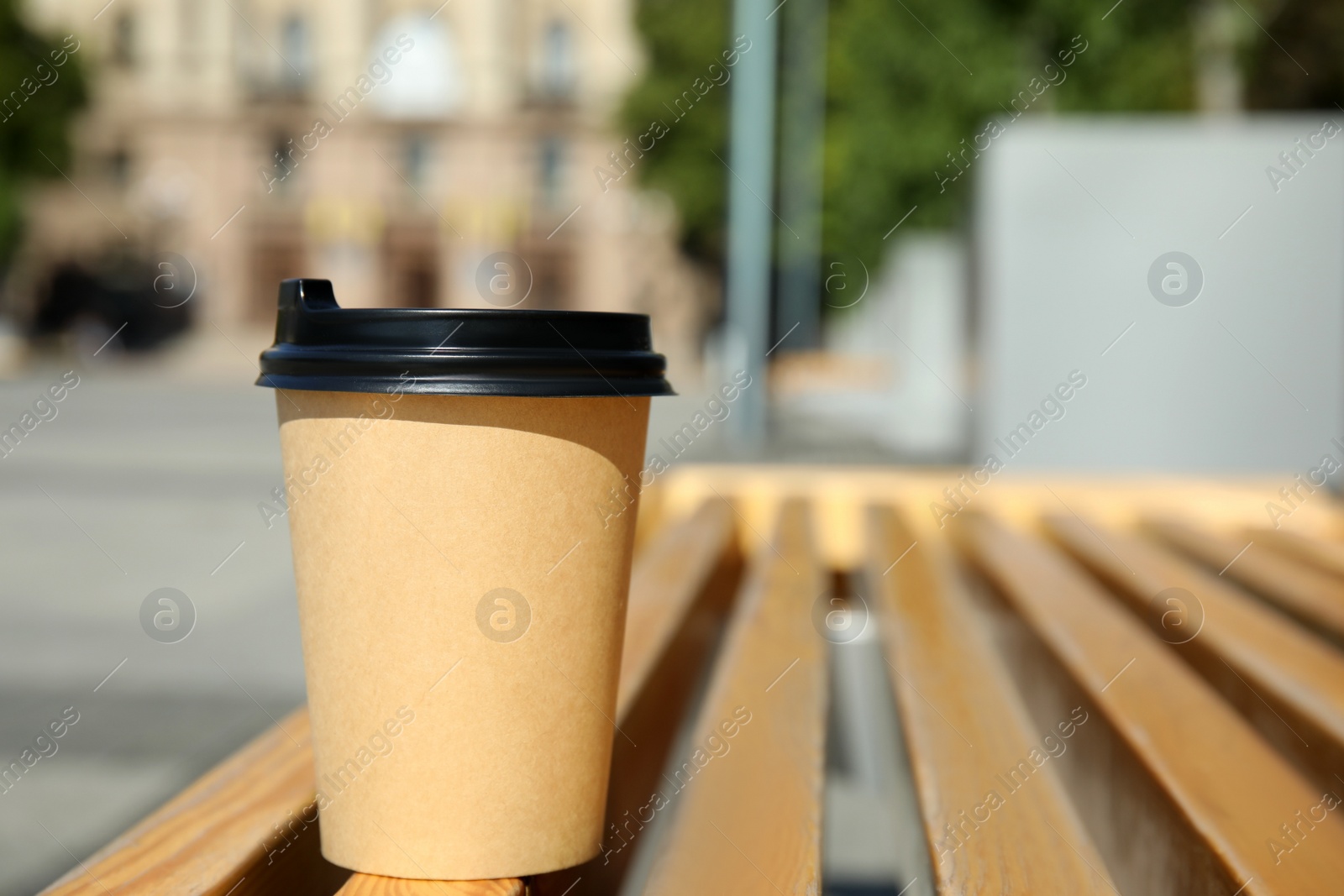 Photo of Takeaway cardboard coffee cup with plastic lid on wooden bench outdoors, space for text