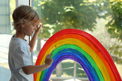 Photo of Little boy drawing rainbow on window. Stay at home concept