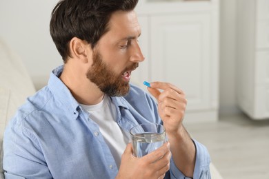 Photo of Handsome man with glass of water taking pill at home, space for text