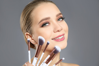Photo of Beautiful woman with makeup brushes on light grey background