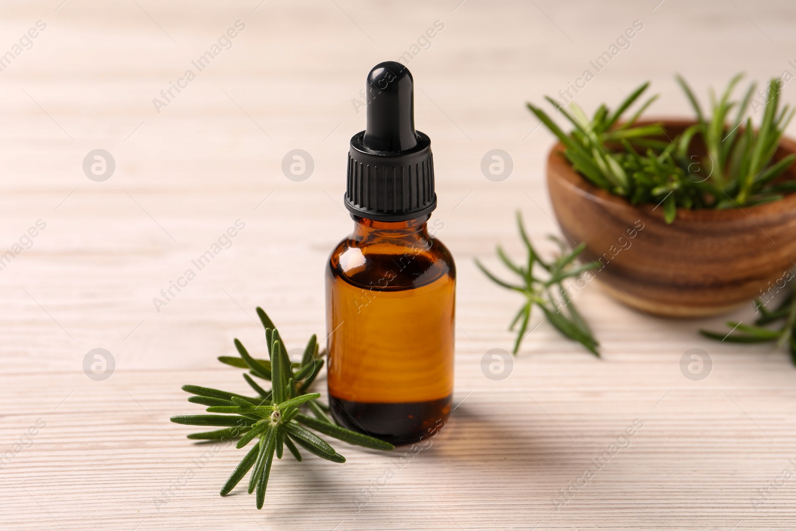 Photo of Bottle with essential oil and fresh rosemary on white wooden table