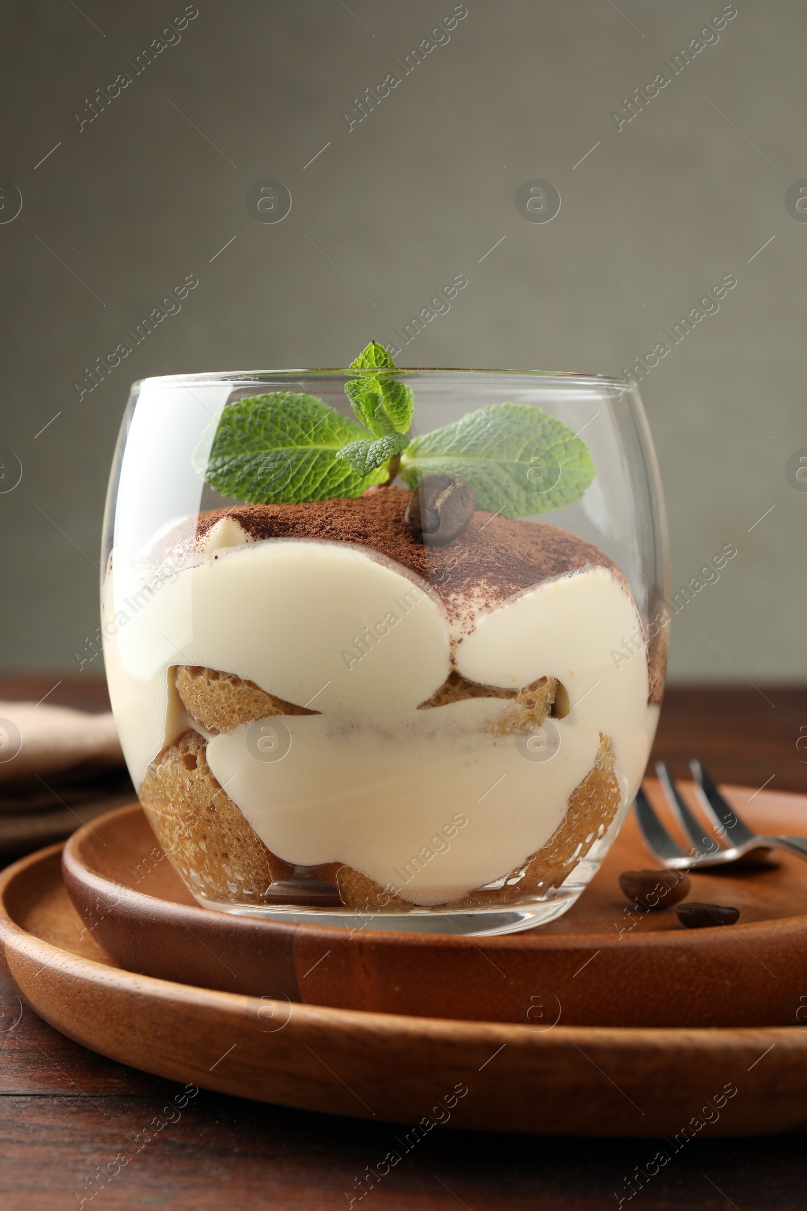 Photo of Delicious tiramisu in glass, mint leaves, coffee beans and fork on wooden table