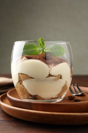 Delicious tiramisu in glass, mint leaves, coffee beans and fork on wooden table