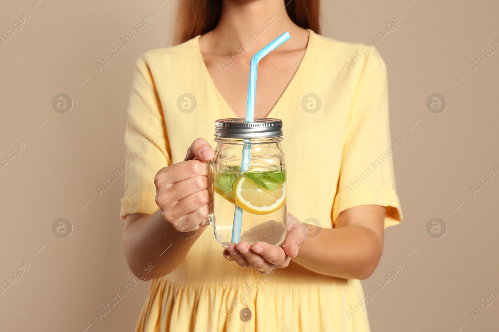 Photo of Young woman with glass of lemon water on beige  background, closeup