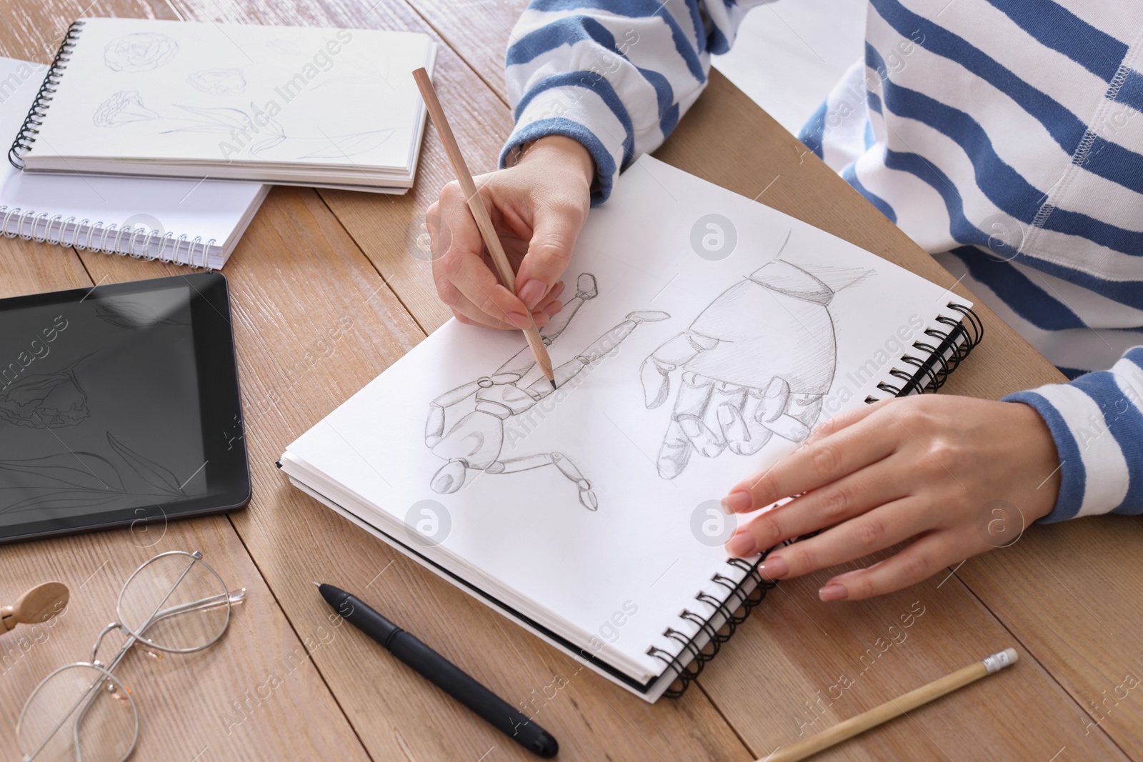 Photo of Woman drawing in sketchbook with pencil at wooden table, closeup