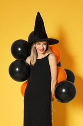 Photo of Beautiful woman wearing witch costume with balloons for Halloween party on yellow background