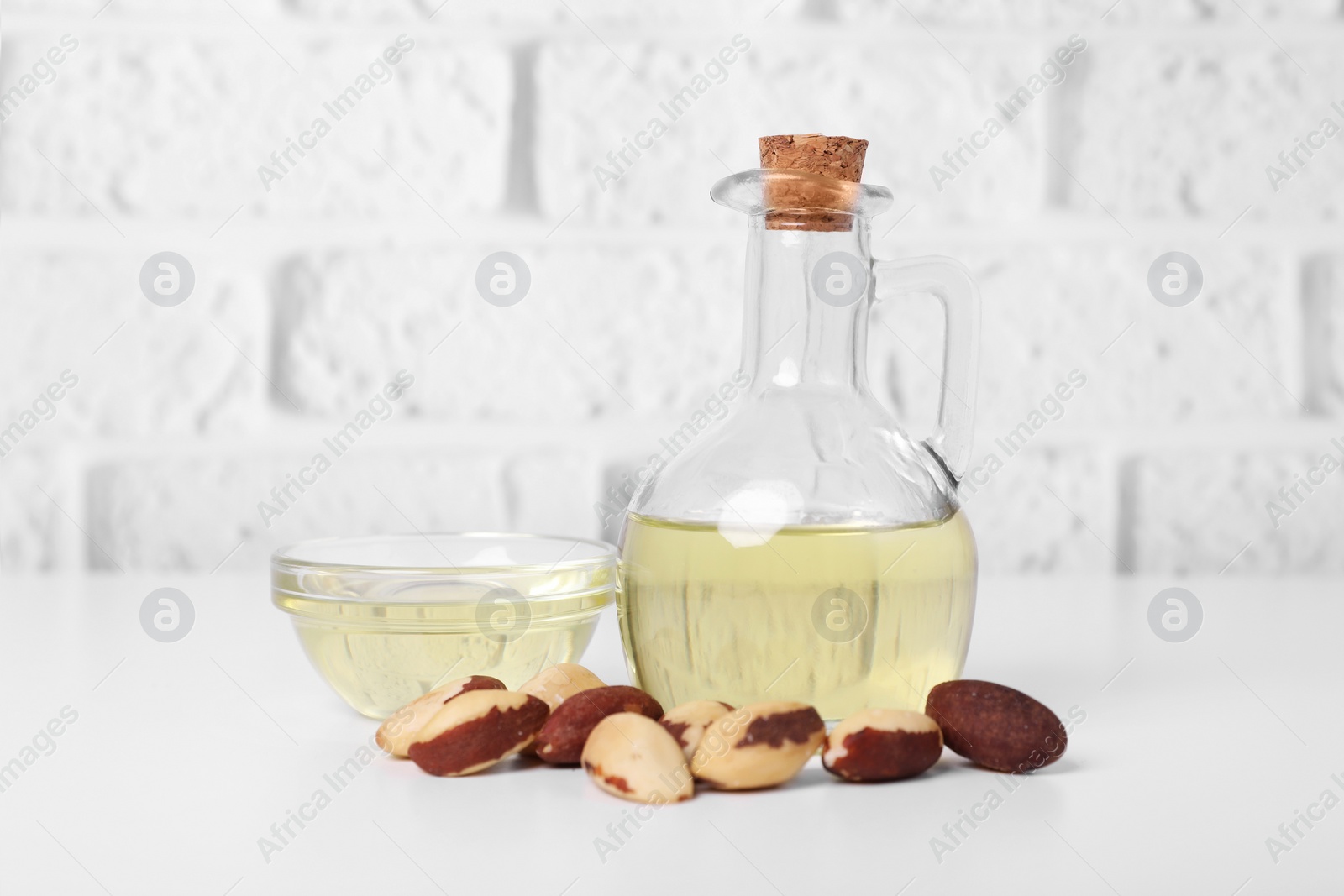 Photo of Tasty Brazil nuts and oil on white table against brick wall