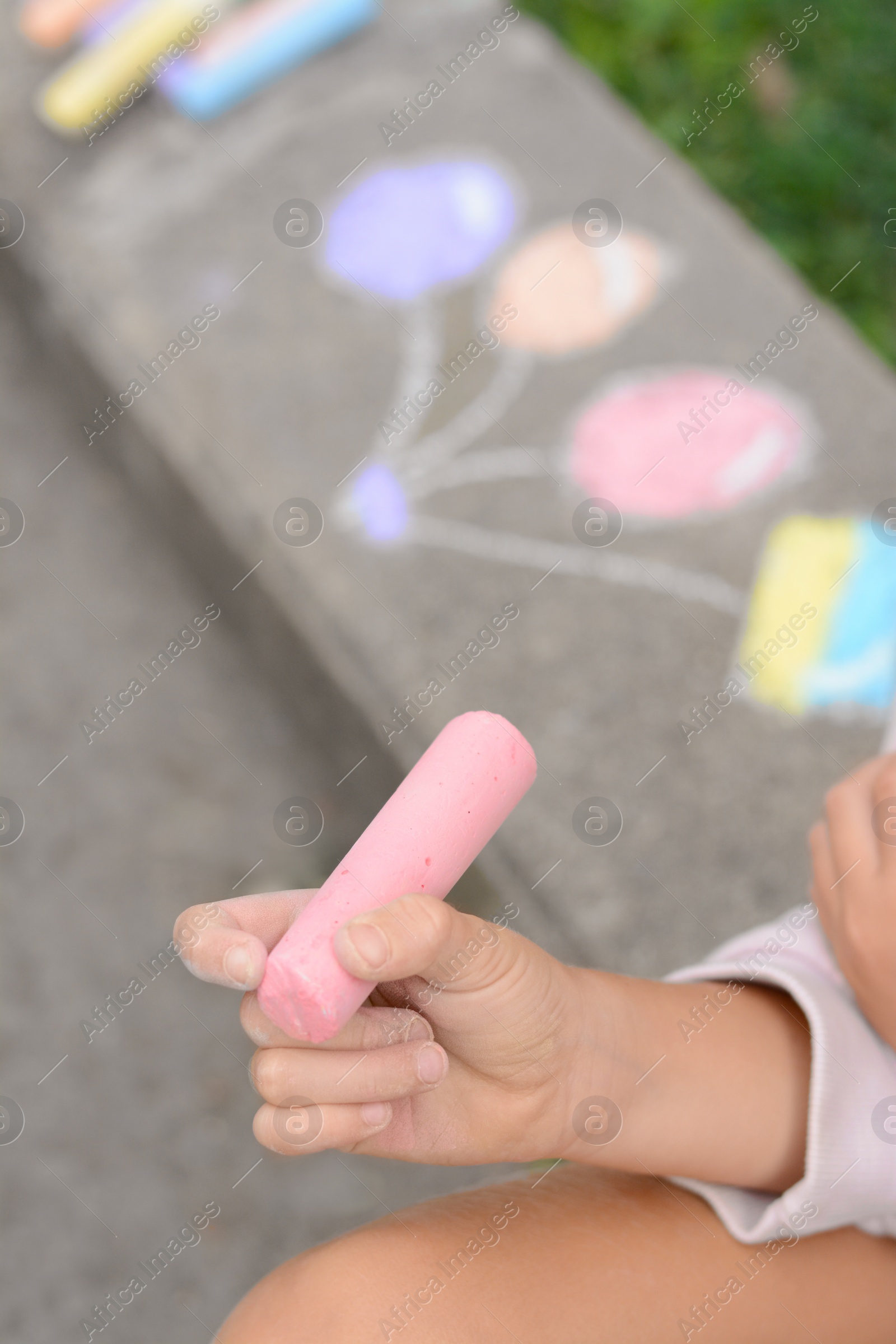 Photo of Little child chalk piece sitting on curb outdoors, closeup. Space for text