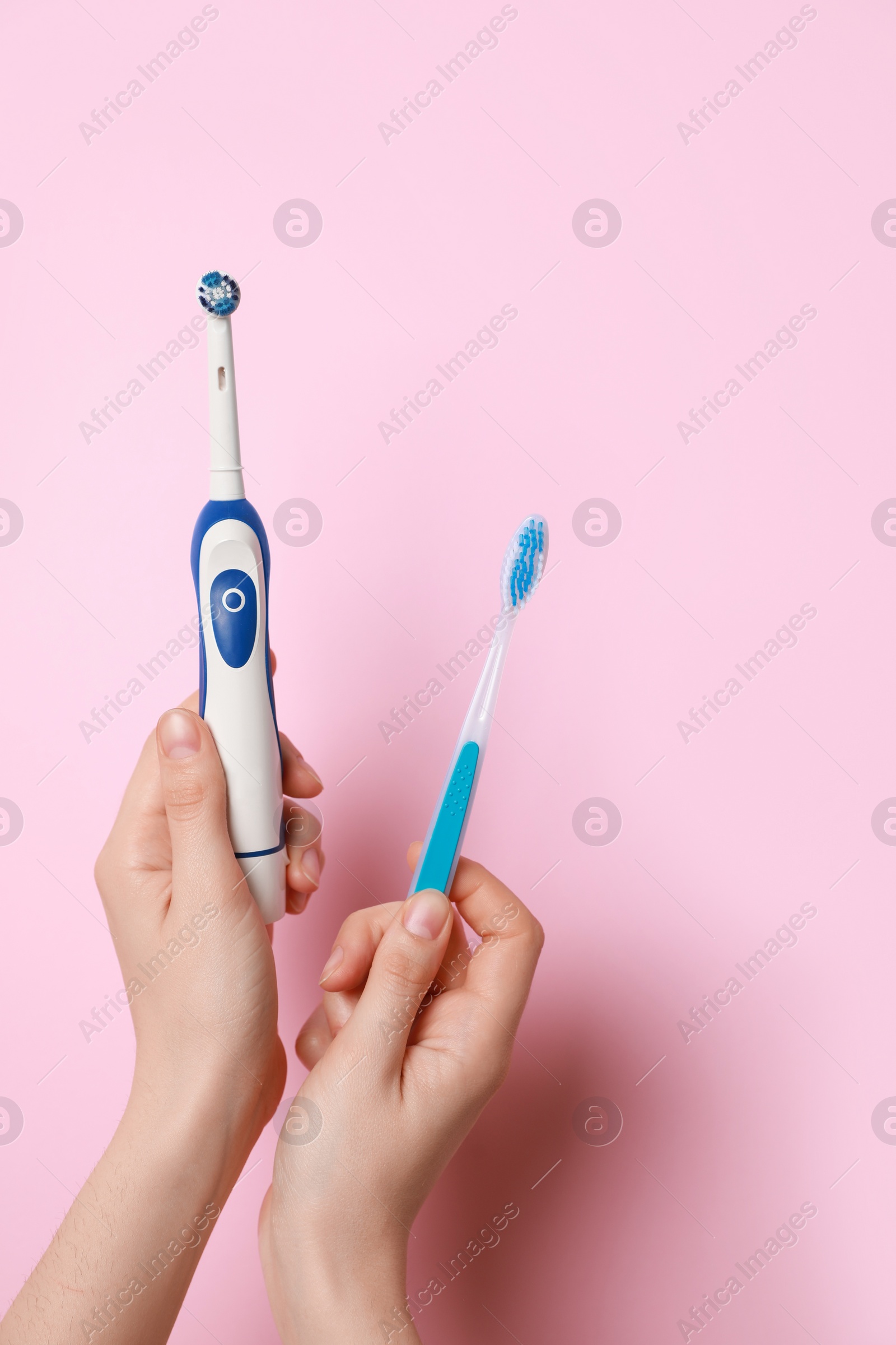 Photo of Woman holding electric and plastic toothbrushes on pink background, closeup