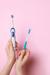 Woman holding electric and plastic toothbrushes on pink background, closeup