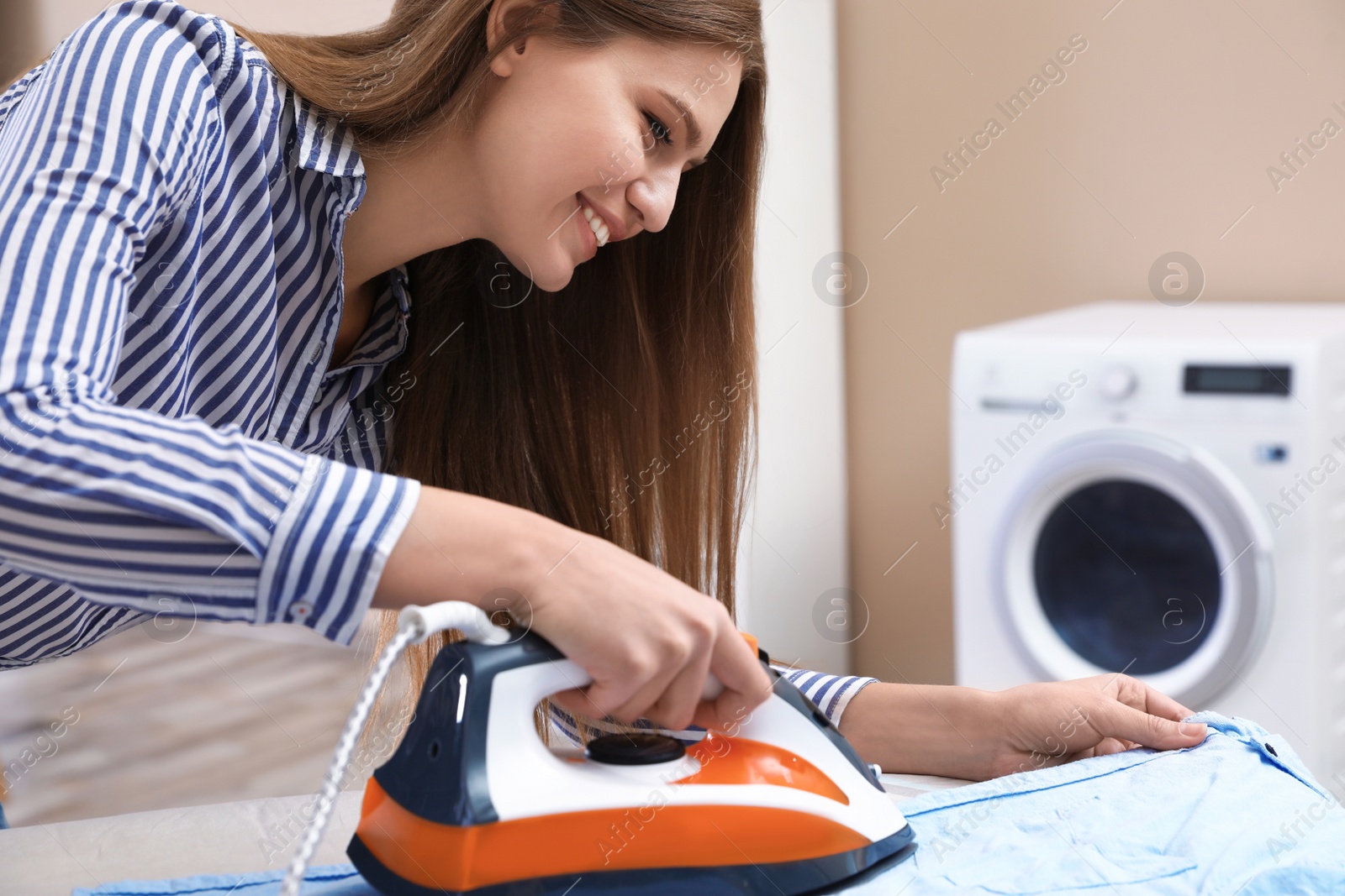 Photo of Young woman ironing shirt on board at home