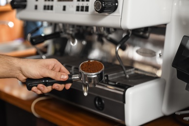 Barista holding portafilter with milled coffee near machine in bar, closeup. Space for text