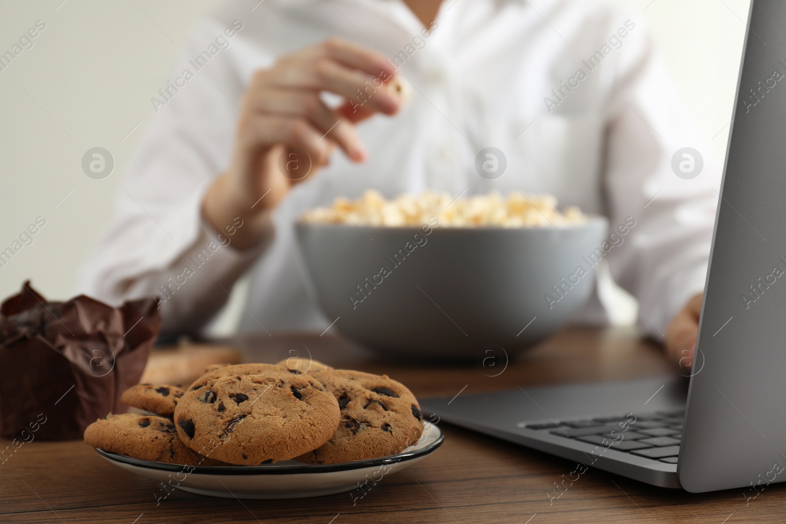 Photo of Bad habits. Woman eating different snacks while using laptop at wooden table, selective focus