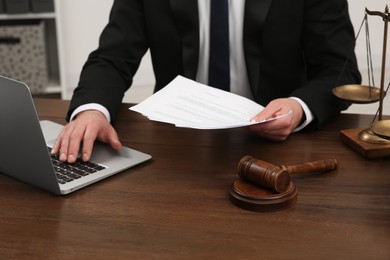 Photo of Law and justice. Lawyer working with documents and laptop at wooden table in office, closeup