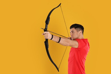 Photo of Man with bow and arrow practicing archery on yellow background