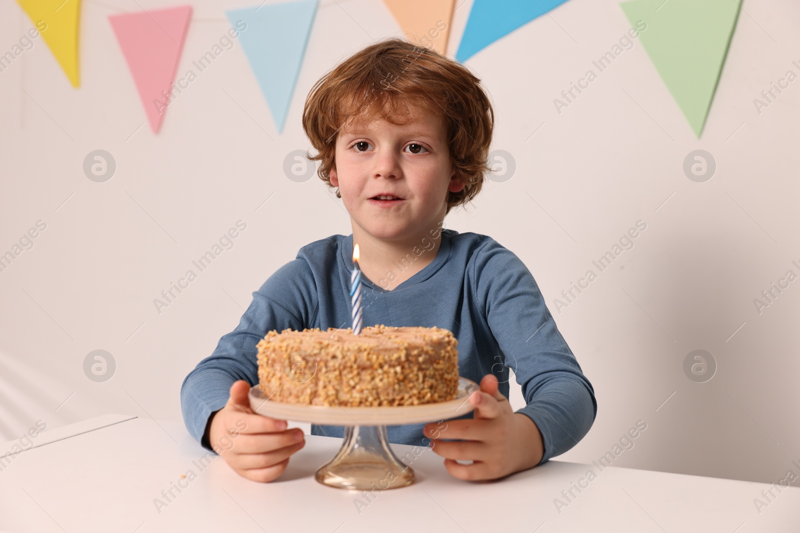 Photo of Cute boy with birthday cake at white table indoors