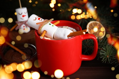 Image of Funny marshmallow snowman in cup with hot drink on wooden table. Bokeh effect 