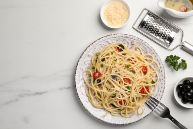 Plate of delicious pasta with olives, tomatoes and parmesan cheese near ingredients on white marble table, flat lay. Space for text