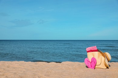 Photo of Summer bag with slippers, beach towel and straw hat on sand near sea, space for text