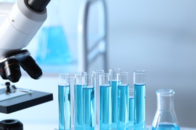 Microscope and test tubes with light blue liquid in laboratory, closeup