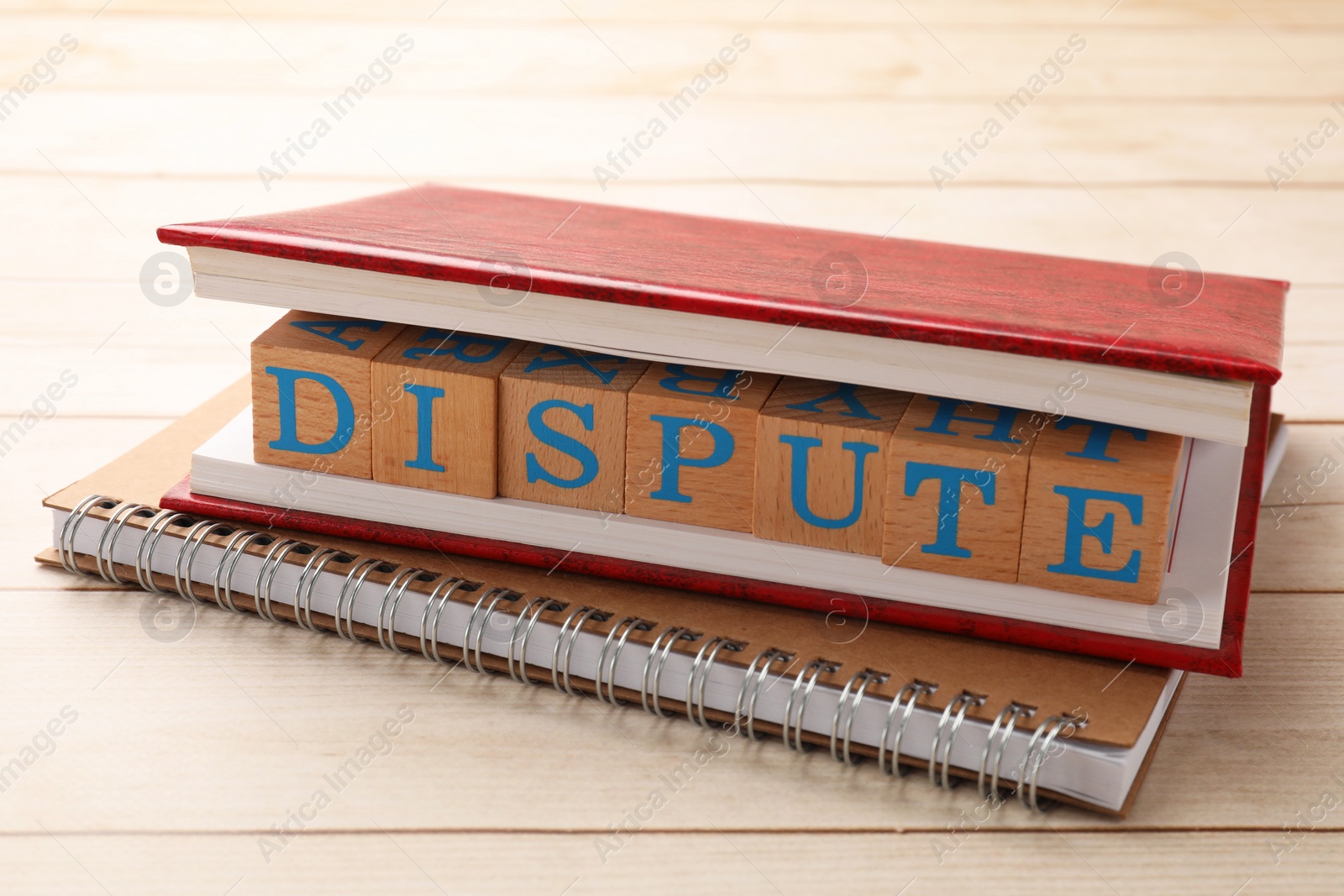 Photo of Cubes with word Dispute and notebooks on wooden table, closeup