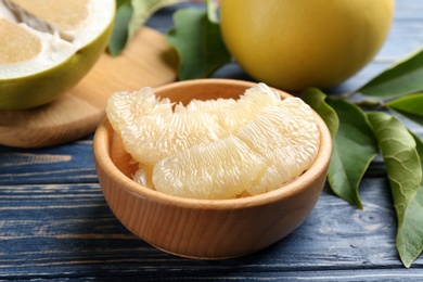 Photo of Bowl with peeled pomelo slices on blue wooden table, closeup