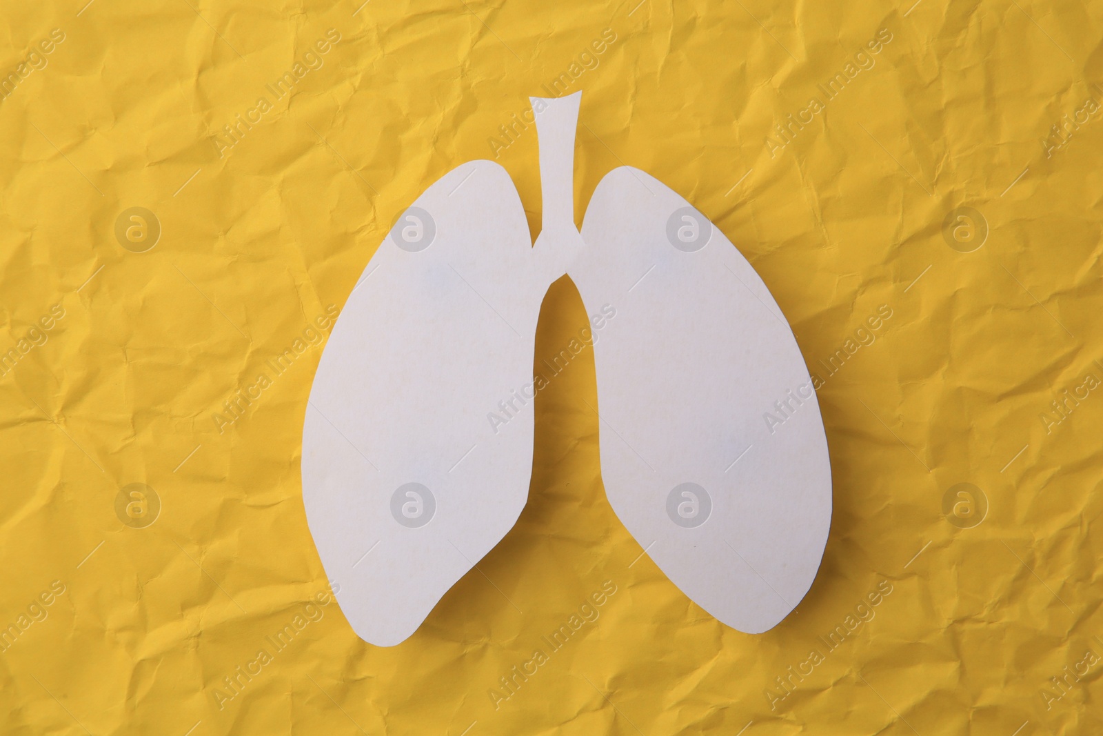 Photo of Paper in shape of human lungs on yellow crumpled background, top view