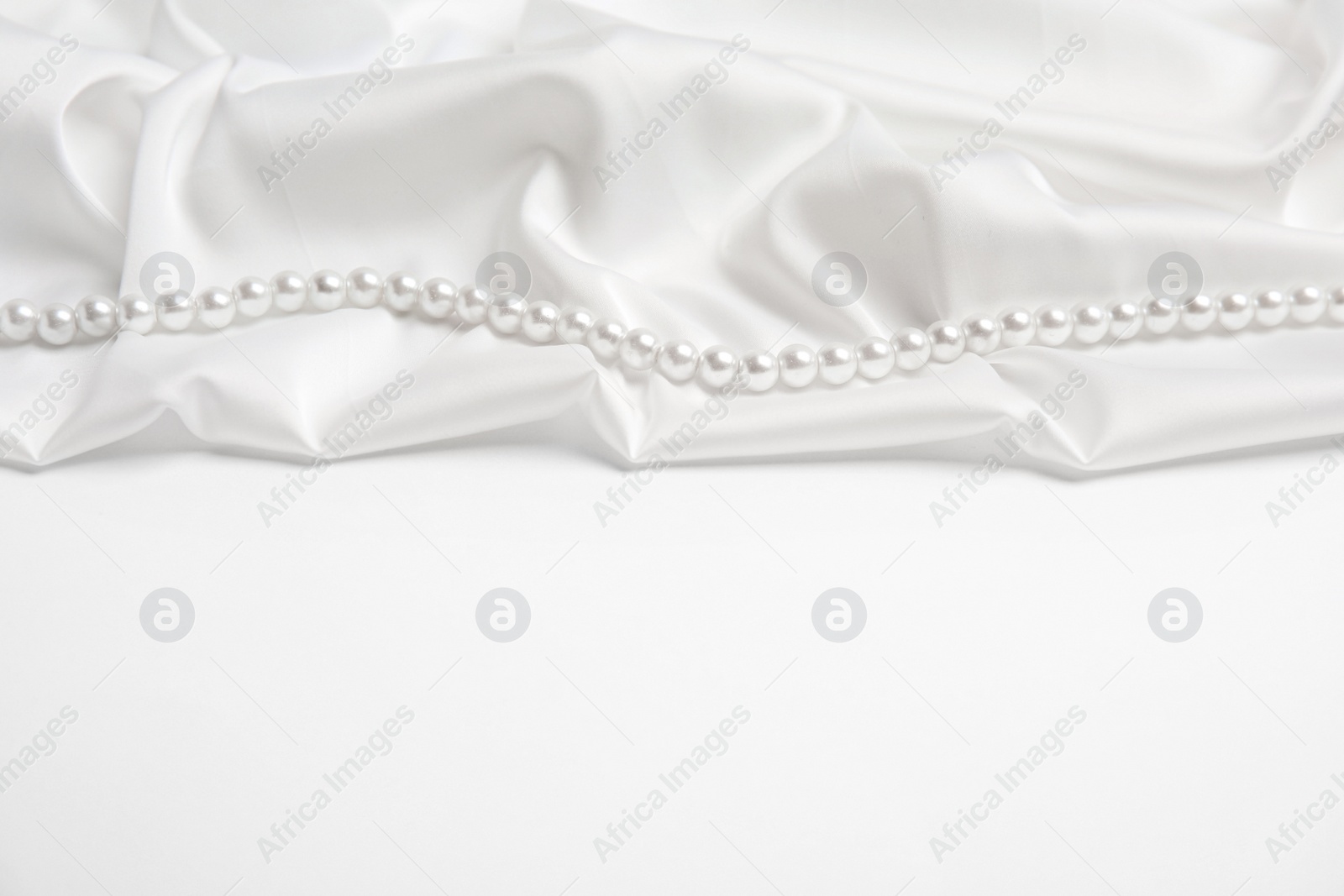 Photo of Beautiful pearls and delicate silk on white background