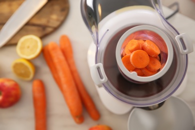 Photo of Modern juicer with fresh slices of carrot on table, top view