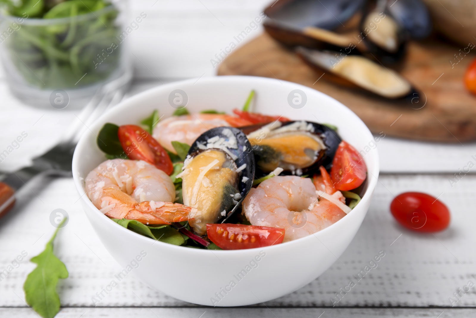 Photo of Bowl of delicious salad with seafood on white wooden table