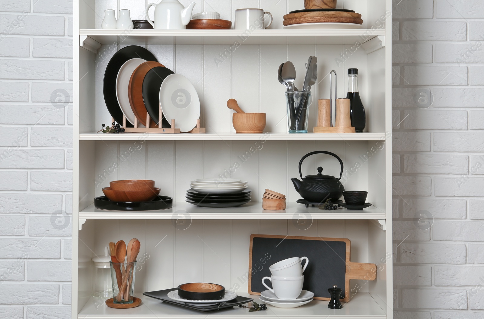 Photo of White shelving unit with set of dishware near brick wall