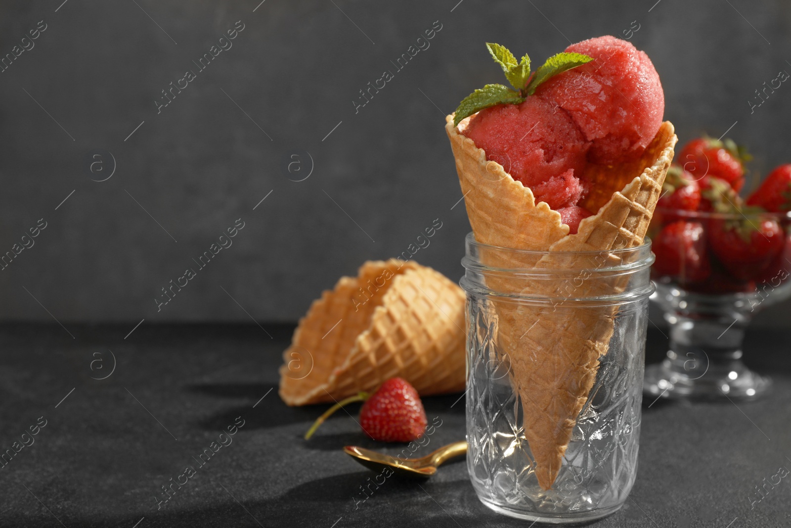 Photo of Delicious strawberry ice cream in wafer cone served on black table, space for text